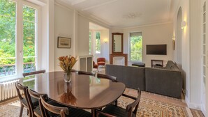 A dining area with a round table, chairs, a vase with flowers, a fireplace, and a sofa.