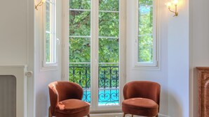 A room with two velvet armchairs, a patterned floor, and a view through a glass door to an outdoor balcony.