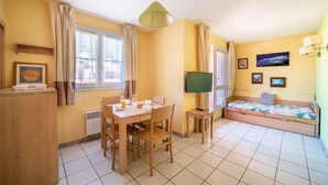 A compact room with a dining table, chairs, a bed, a television, and a small table with a lamp. - Le Cap et la Mer - Vue Mer (Cerbere)