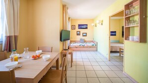 A room with a bed, a TV, a dining table with chairs, and a breakfast setup. - Le Cap et la Mer - Vue Mer (Cerbere)
