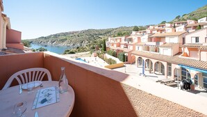 A terrace with a table set for dining, overlooking a coastal area with buildings and a clear sky. - Le Cap et la Mer - Vue Mer (Cerbere)
