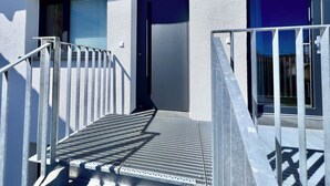 A modern building with a metal staircase leading to a door, a small window with blinds, and a metal railing.