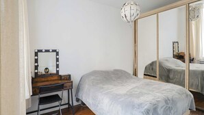 Un dormitorio con cama, tocador con espejo e iluminación, y armario con espejo.