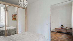 Una habitación minimalista con una cama, un armario y un pequeño banco de madera.
