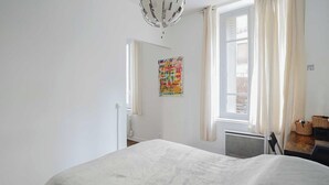 Un dormitorio con cama, un radiador, una ventana con cortinas y una puerta que da a otra habitación.