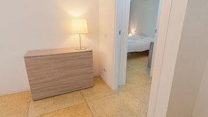 A bedroom with a bed, a bedside table with a lamp, and a wooden dresser. - 16 Relais du Lac Elite (Desenzano del Garda)
