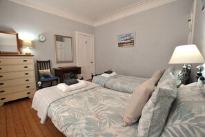 Een slaapkamer met twee bedden, een kapstok, een stoel, een lamp, een klok en een deur.