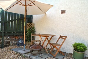 Een terras buiten met een tafel, stoelen, een vuurkorf en een plant in pot.