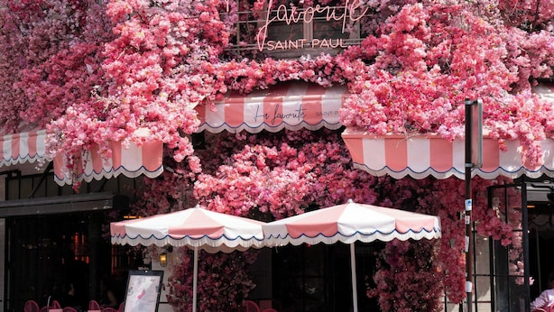 Una cafetería con decoración floral rosa y mesas al aire libre.