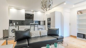 Una sala de estar moderna con un sofá de cuero negro, una mesa de centro de vidrio y una cocina al fondo.