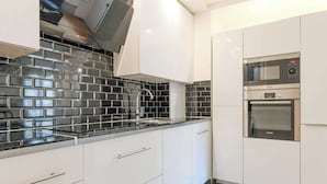 Una cocina moderna con gabinetes blancos, salpicadero de baldosas negras y electrodomésticos de acero inoxidable, incluyendo un horno Bosch.