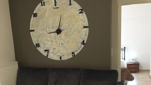 Ein Wohnzimmer mit Ecksofa, einer großen Wanduhr und einer Heizung.