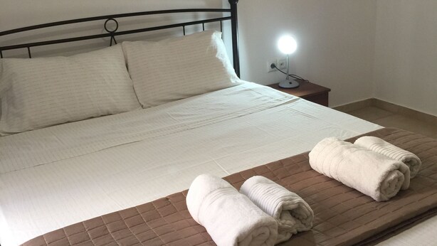 Ein ordentlich bezogenes Bett mit einer braunen gesteppten Tagesdecke, zwei aufgerollten Handtüchern und einer Nachttischlampe.