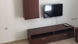 Ein Wohnzimmer mit an der Wand montiertem Fernseher, einem Holzschrank darunter und einem kleinen Regal mit Dekorationen.