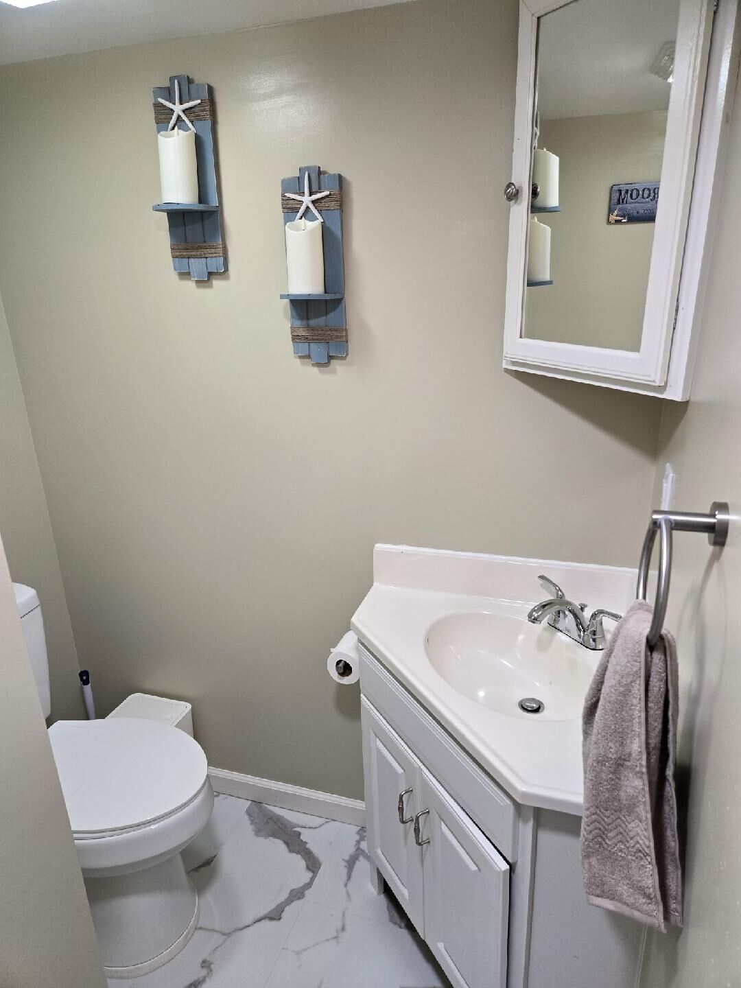 Een badkamer met toilet, wastafel en een wastafelmeubel. Er zijn twee handdoekrekken aan de muur en een spiegel boven de wastafel.