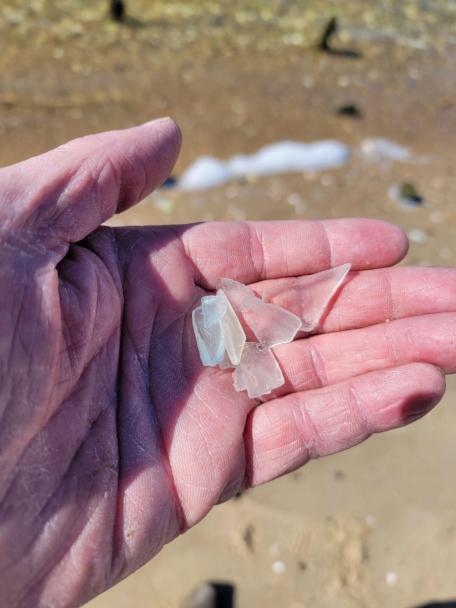 Una mano che tiene cristalli trasparenti su una spiaggia sabbiosa.