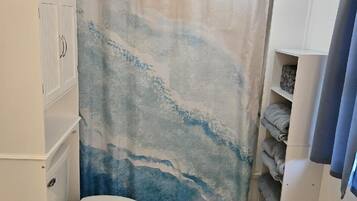 A bathroom with a toilet, a towel rack, a shower curtain, and a small shelf.
