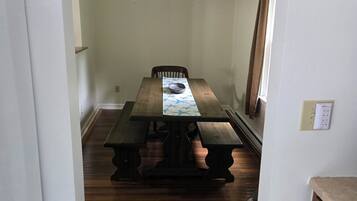 A dining area with a wooden table and benches, a ceiling light fixture, and a window with curtains.