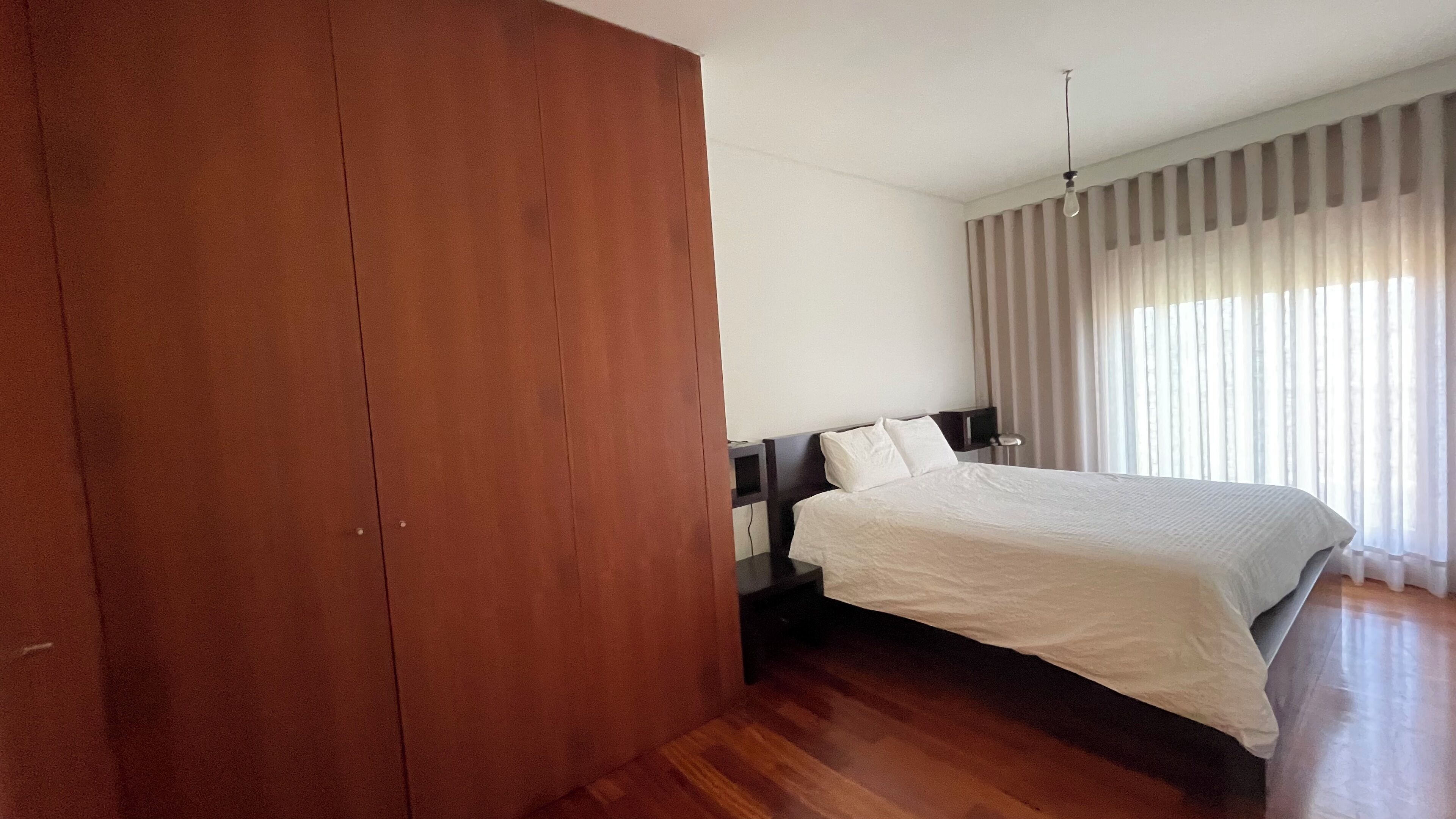Ein Schlafzimmer mit großem Holzschrank, einem Bett mit weißer Bettwäsche, einem Nachttisch und einem Fernseher.