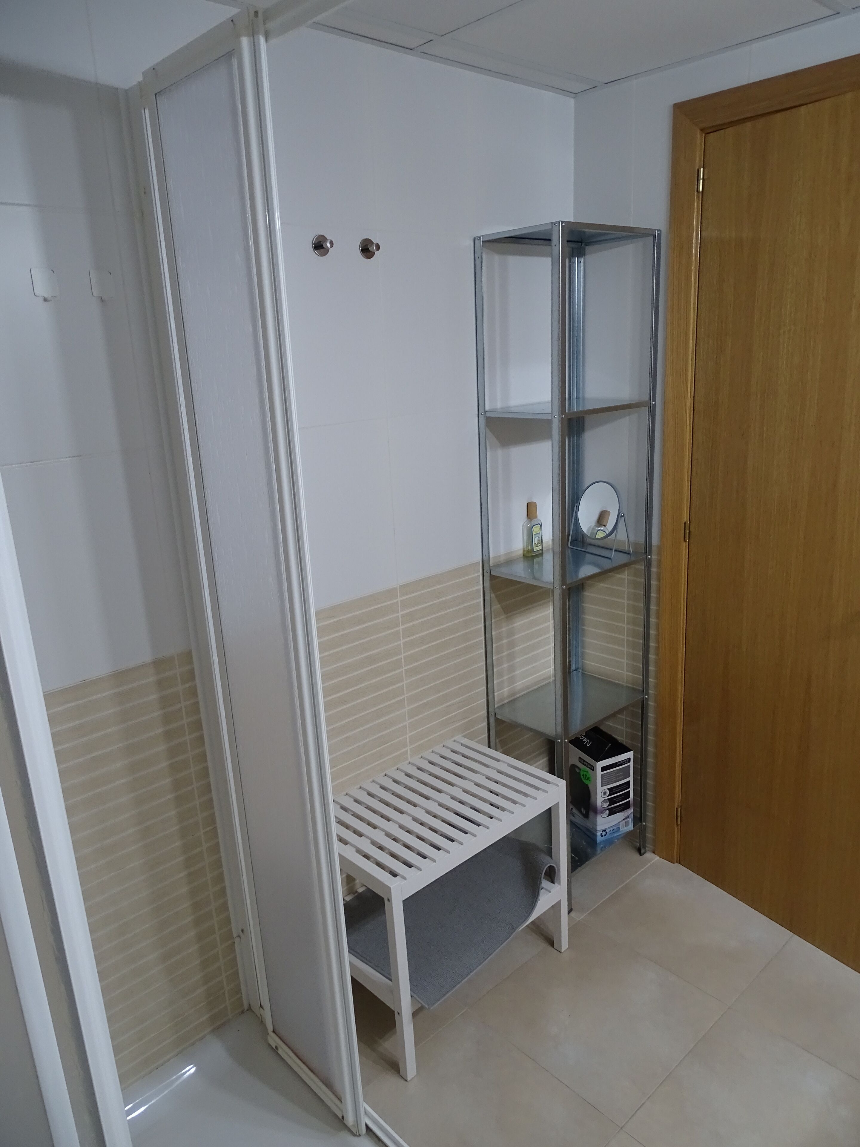 A room with a white bench, a glass shelving unit, and a wooden door.