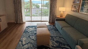 A living room with a blue sofa, a matching ottoman, a lamp, and a view of a balcony with a railing. - Best Resort in Naples, FL,Old Town,Ideal location 2BD/2BA,Property overlooks Bay (Naples)