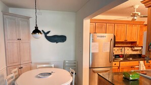 Una cocina con armarios de madera, un refrigerador de acero inoxidable, una mesa de comedor con sillas y una decoración de ballena en la pared.
