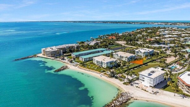 Vista aérea de un complejo turístico costero con varias edificaciones, una playa y aguas azul turquesa.
