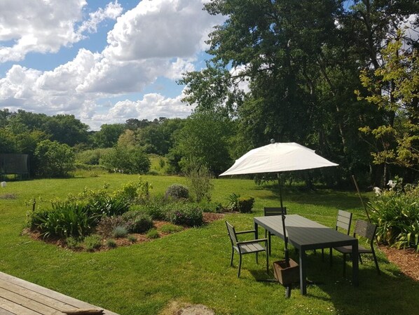 An outdoor patio with a table and chairs, surrounded by a lush garden and trees.