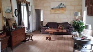 A spacious living room with a high ceiling, wooden beams, a sofa, a dining table, and a small dog.