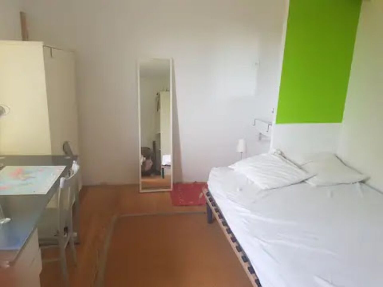 A room with a bed, a desk, and a mirror.