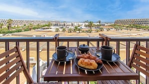 En balkong med ett bord dukat för frukost, med utsikt över en stadssiluett med moderna byggnader och palmer.