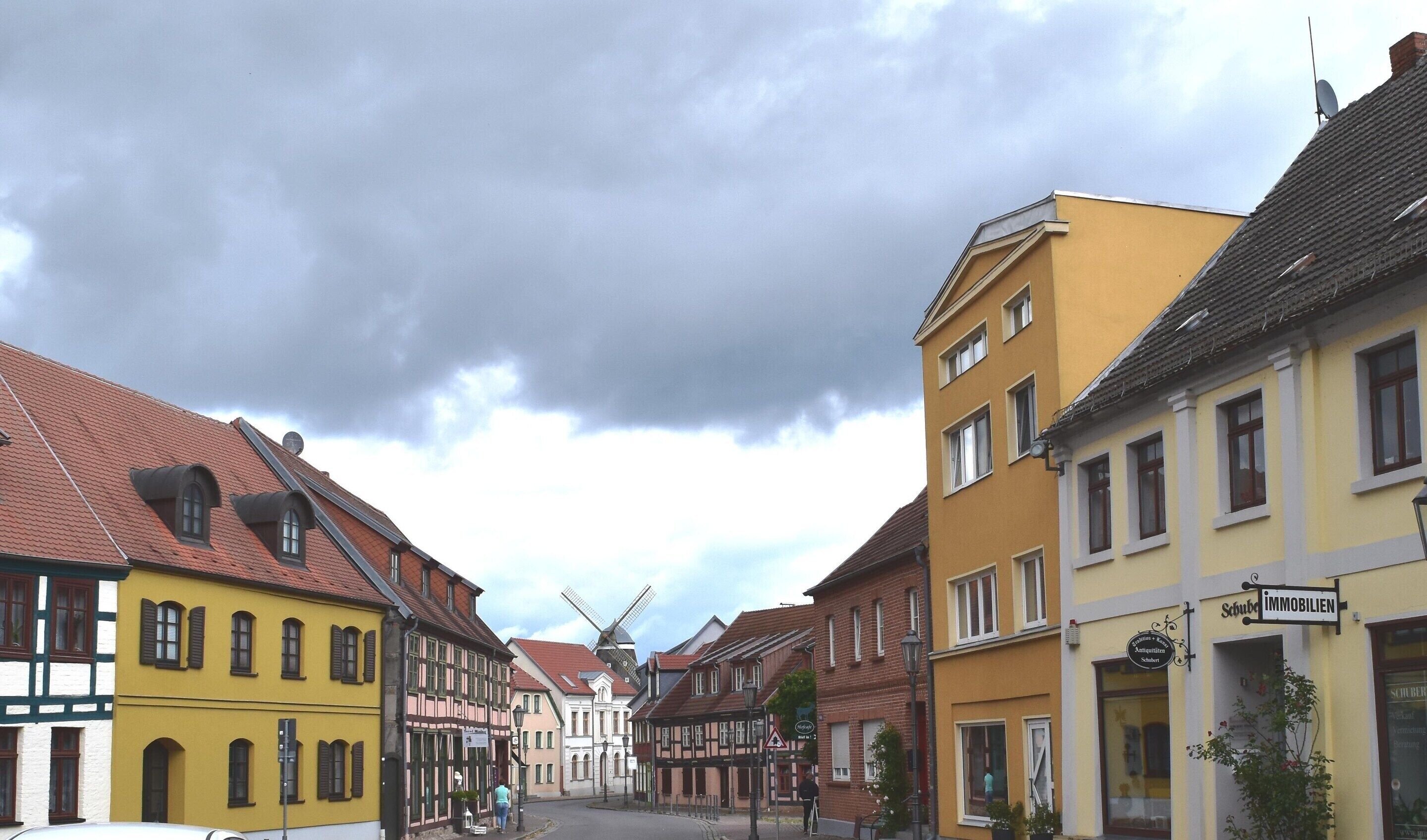A street lined with traditional European buildings, including a yellow building with a sign for 'Schule Immobilien'.
