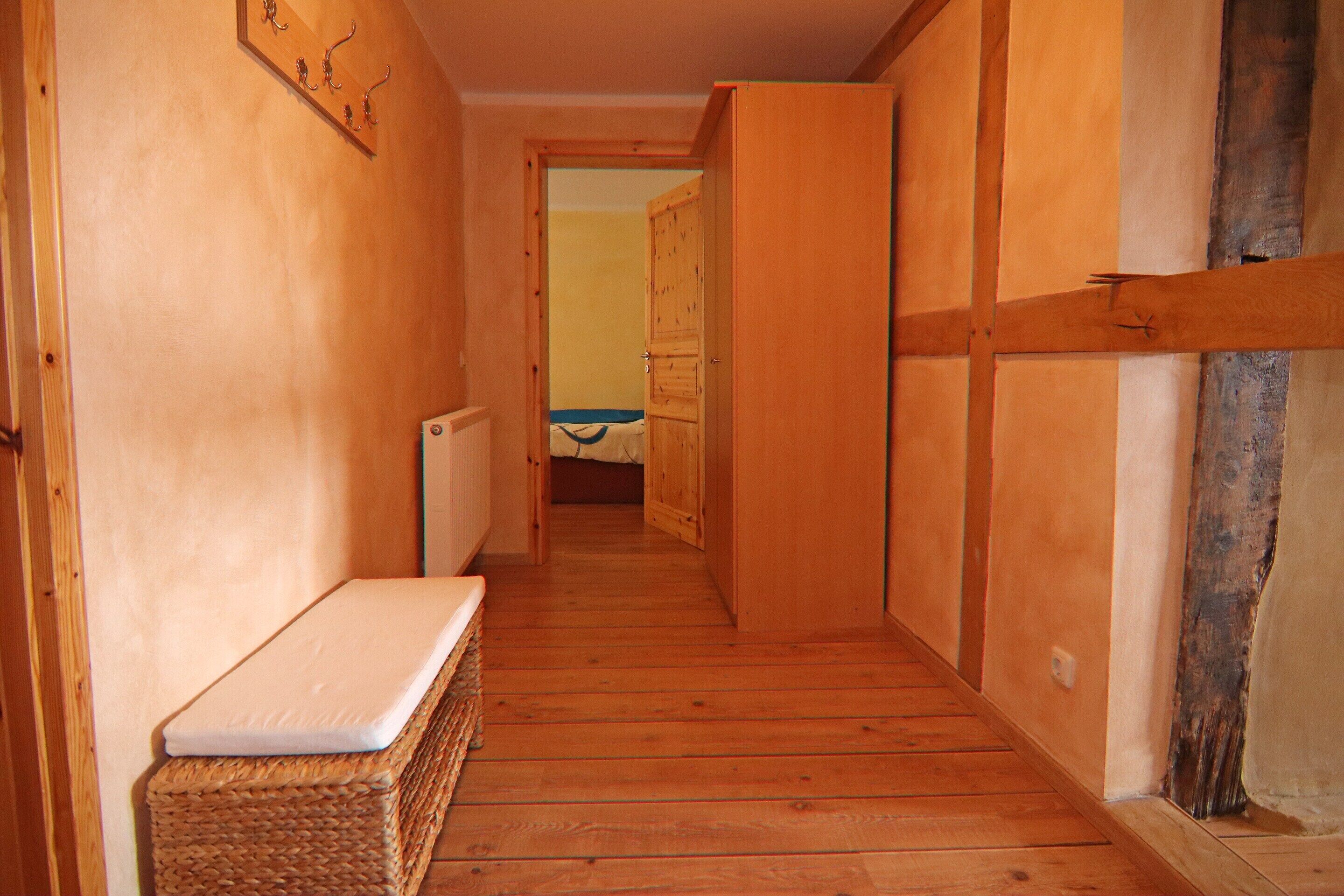 A narrow hallway with wooden walls and floors, leading to a room with a bed and a window.