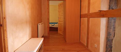 A narrow hallway with wooden walls and floors, leading to a room with a bed and a window.