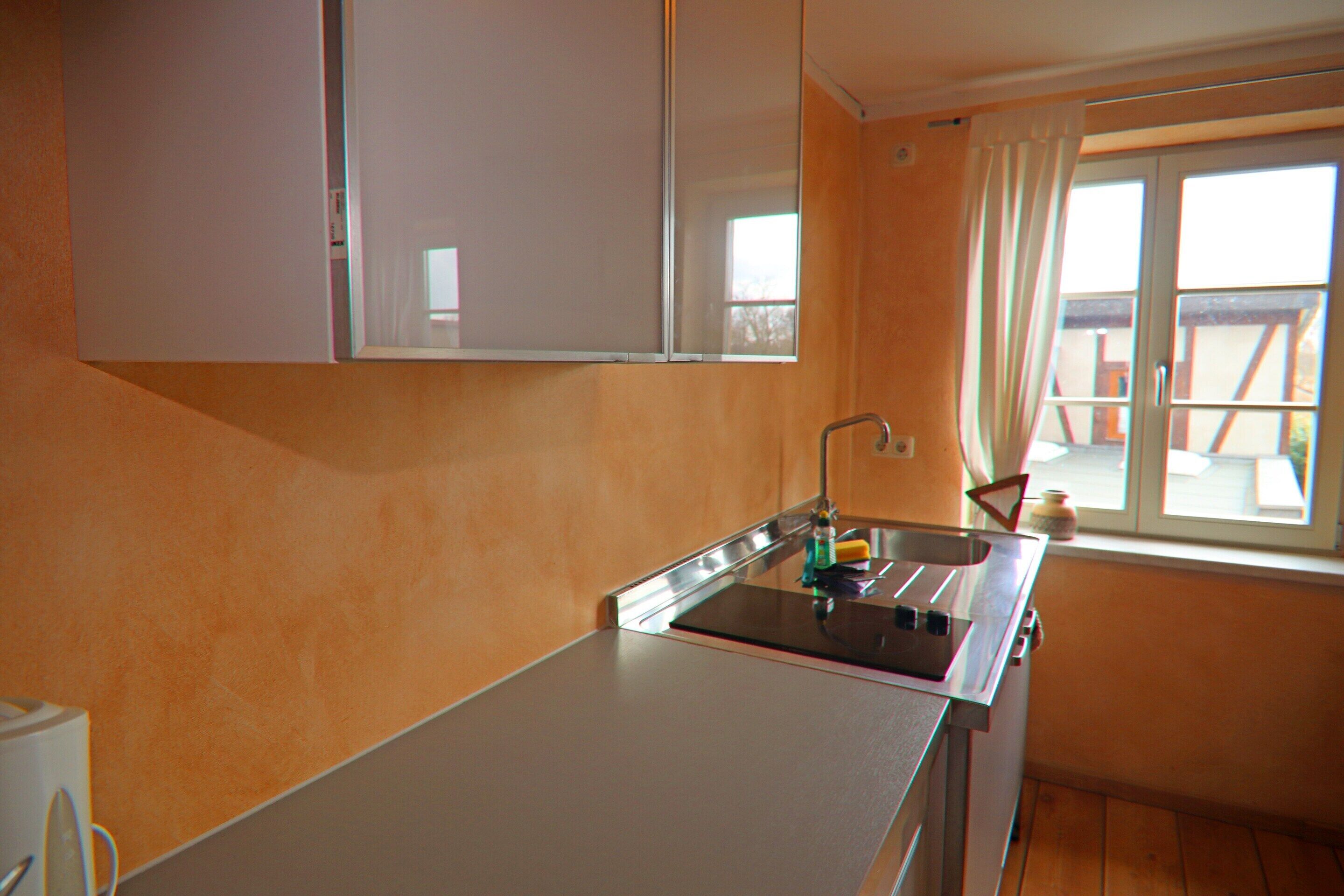 Una cocina con un lavamanos, armarios y una ventana con cortinas.