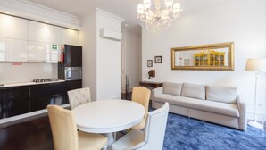 Una sala moderna con una mesa redonda blanca y sillas color beige, un sofá color beige, y una lámpara de araña.