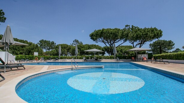 Une piscine de forme circulaire, entourée de chaises longues et de parasols.