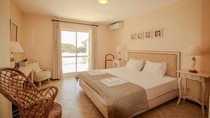 Une chambre d’hôtel avec un grand lit, un fauteuil en osier, une petite table et une vue sur l’extérieur.