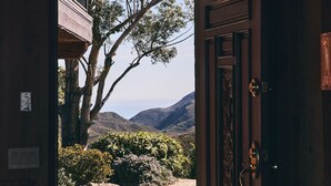 An open wooden door leading to a paved outdoor area with a view of mountains and trees. - FIVE MINUTES TO CALAMIGOS RANCH AND CEILO FARMS MOUNTAIN AND OCEAN VIEWS (Malibu)