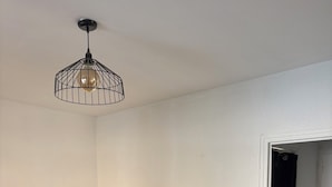 A room with a sofa, a wooden table, a hanging light fixture, a radiator, and a door leading to another room.
