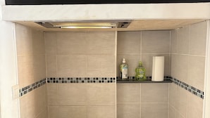 A compact kitchen with a built-in stove, sink, and a small shelf with cleaning supplies.