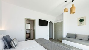A modern bedroom with a large bed, a built-in bench, a TV, and a door leading to a bathroom. - Phaedrus Living: Paros Cycladic Residences 7 (Paros)