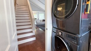 A laundry area with a front-loading washer and dryer, a wooden staircase leading to a living area, and a view of the outdoors. - The PennHaus - Peaceful Home Near Lake CDA & Shops (Coeur d'Alene)