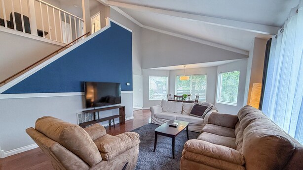 A living room with a staircase, a flat-screen TV, two sofas, and a dining area with a table and chairs. - The PennHaus - Peaceful Home Near Lake CDA & Shops (Coeur d'Alene)