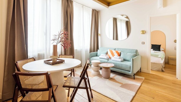 A modern living room with a round dining table, two chairs, a sofa, and a mirror. - Port-royal Residence - Cosy Apartment - 1br- 4P (Paris)