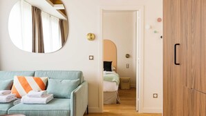 A modern hotel room with a light green sofa, a round mirror, a wooden wardrobe, and a bed with a green and white duvet. - Port-royal Residence - Cosy Apartment - 1br- 4P (Paris)