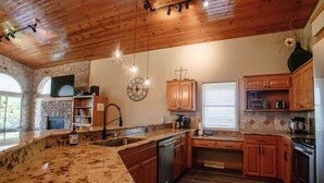 A kitchen with granite countertops, wooden cabinets, a stone fireplace, and a large clock on the wall. - Direct access to the lake, short drive to all the Branson fun! (Kimberling City)