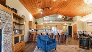 A spacious living area with a blue sofa, wooden bookshelves, and a kitchen with a central island. - Direct access to the lake, short drive to all the Branson fun! (Kimberling City)