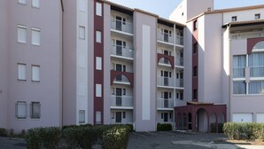 Un immeuble résidentiel à plusieurs étages, doté de balcons, d’un espace de stationnement et d’un petit jardin.