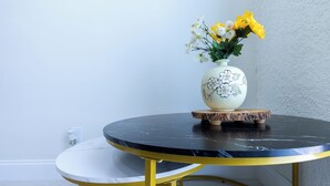 Een ronde tafel met een witte marmeren blad en gouden poten, vergezeld van een witte vaas met bloemmotieven en gele bloemen.